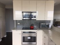 Design Craft Cabinets in Eaton Flat Door style with High Gloss Pearl thermafoil. Stainless Steel toe kicks. Quartz countertops in Off White.
