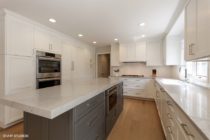Kitchen features gray island with white surrounding cabinets.